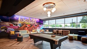 A pool table in a room with a mural of a cityscape and the word "Louisville" on the wall. - Tru by Hilton Louisville Airport (Louisville)