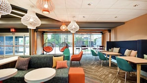 A modern interior with seating areas, tables, and hanging light fixtures. - Tru by Hilton Louisville Airport (Louisville)