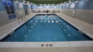 An indoor swimming pool with clear water, marked depth lines, and safety signs.