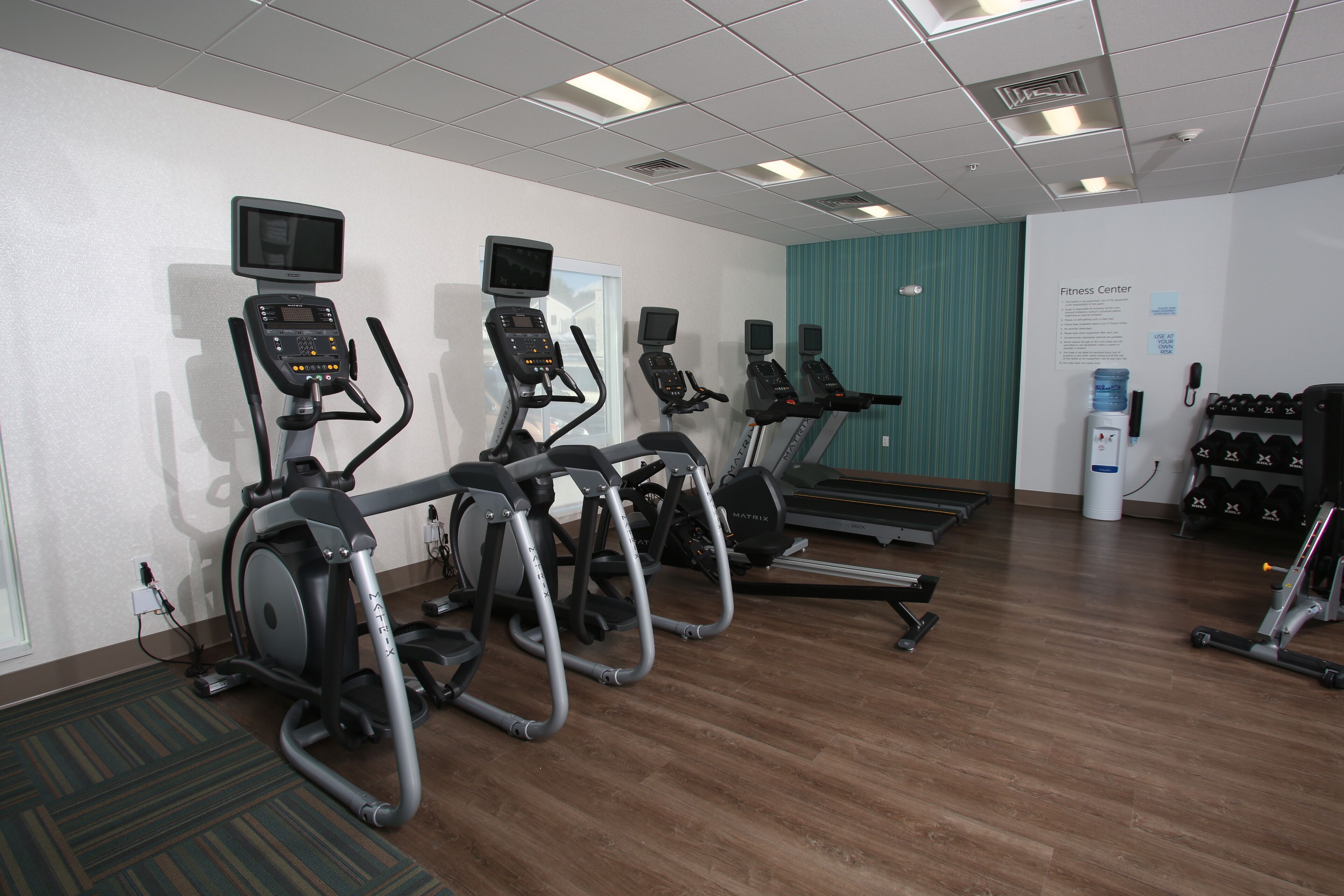A fitness center with treadmills, ellipticals, and a wall-mounted screen.