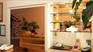 A hotel reception area with a glass display case, a telephone, and various decorative items including plants and flowers. - Hotel Ristorante Grappolo D'Oro (Pietrasanta)