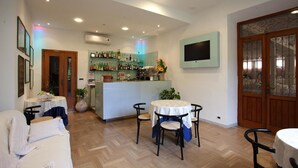 A cozy living area with a dining table, a bar area with a variety of bottles, and a TV mounted on the wall. - Hotel Ristorante Grappolo D'Oro (Pietrasanta)