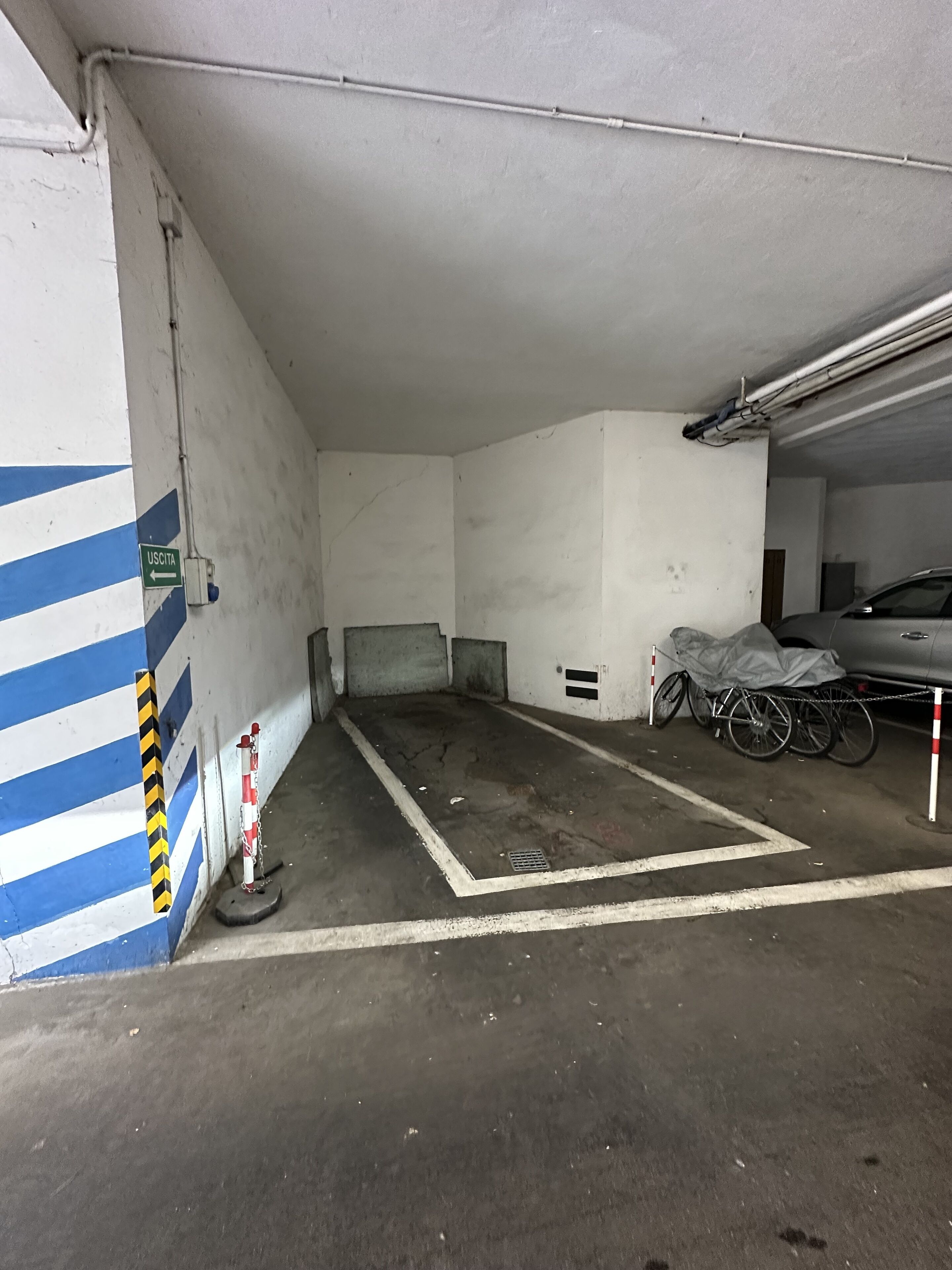 A parking garage with a blue and white striped wall, a sign indicating 'USCITA', and a bicycle parked near the wall.