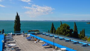 Una terraza con sillones de sol y mesas con vista a un cuerpo de agua.