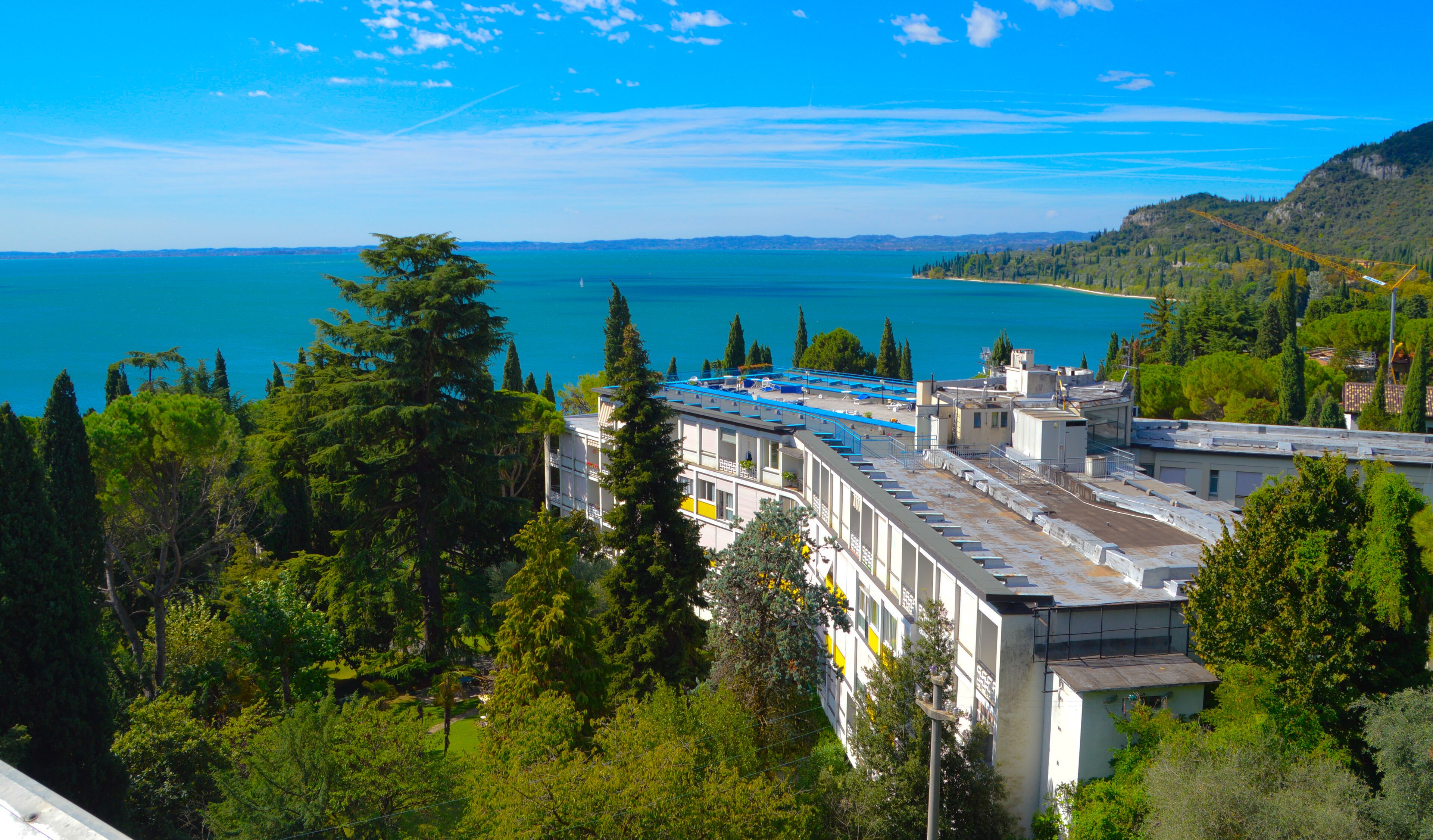 A hotel with a rooftop terrace overlooking a body of water and a hilly landscape.