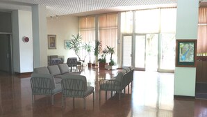 Un vestíbulo amplio con sofá, sillas, plantas en macetas y un gran ventanal con cortinas.