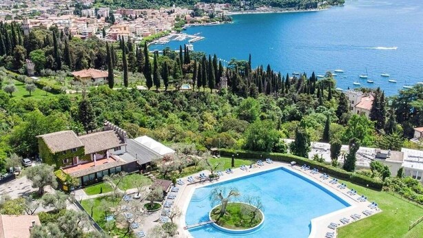 Un resort con una gran piscina rodeada de sillones de descanso, vistas al mar y montañas al fondo.