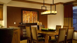 Uma sala de jantar com uma mesa de madeira, cadeiras, um candelabro e um quadro na parede.