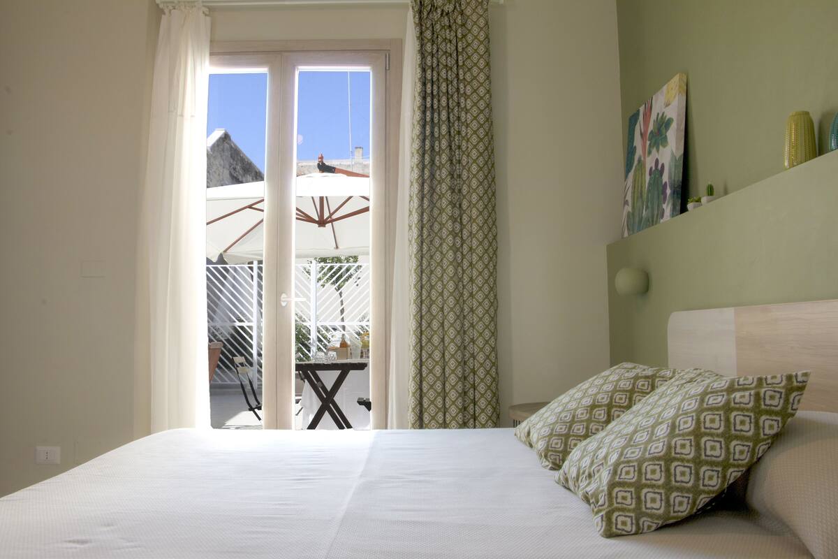 A bedroom with a bed, a view of the balcony, and a painting on the wall.