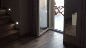 Una habitación con una escalera de madera y un ventanal corredera que da a un espacio exterior con terraza de madera.