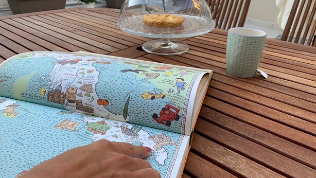 Un libro abierto sobre una mesa de madera con un mapa y una campana de vidrio sobre una galleta.