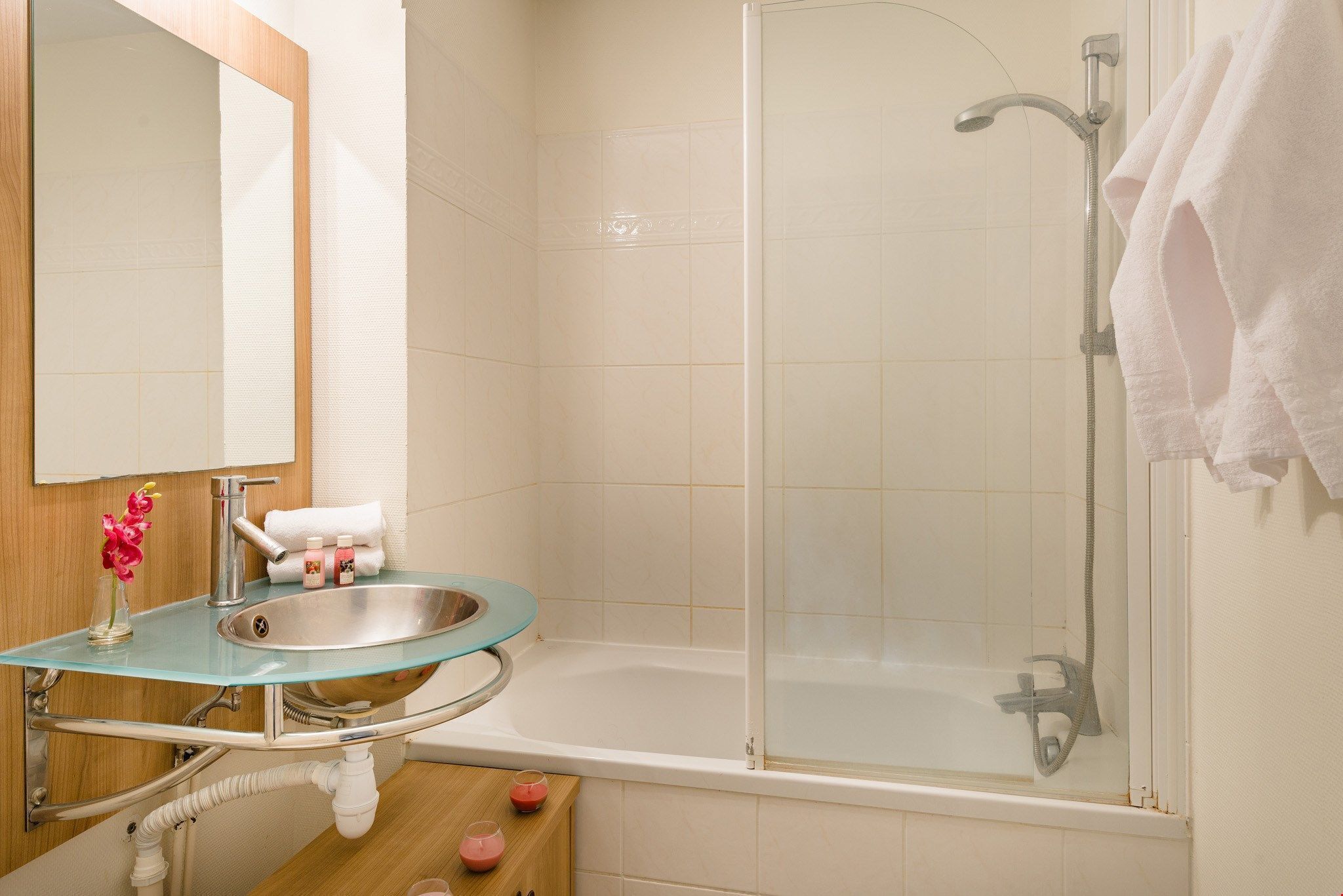 A bathroom with a glass sink, a mirror, a bathtub, and a shower.