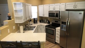 Una cocina moderna con armarios blancos, electrodomésticos de acero inoxidable, una cafetera y un lavamanos.