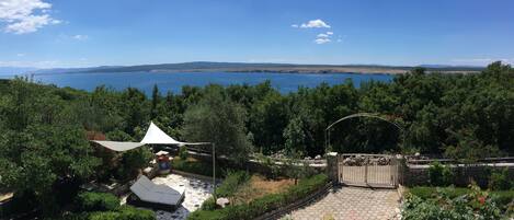 Un patio con toldo blanco, suelo de piedra y vista al mar.