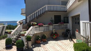 Un edificio de varios pisos con una escalera que lleva a un balcón, rodeado de plantas en macetas y una bicicleta.