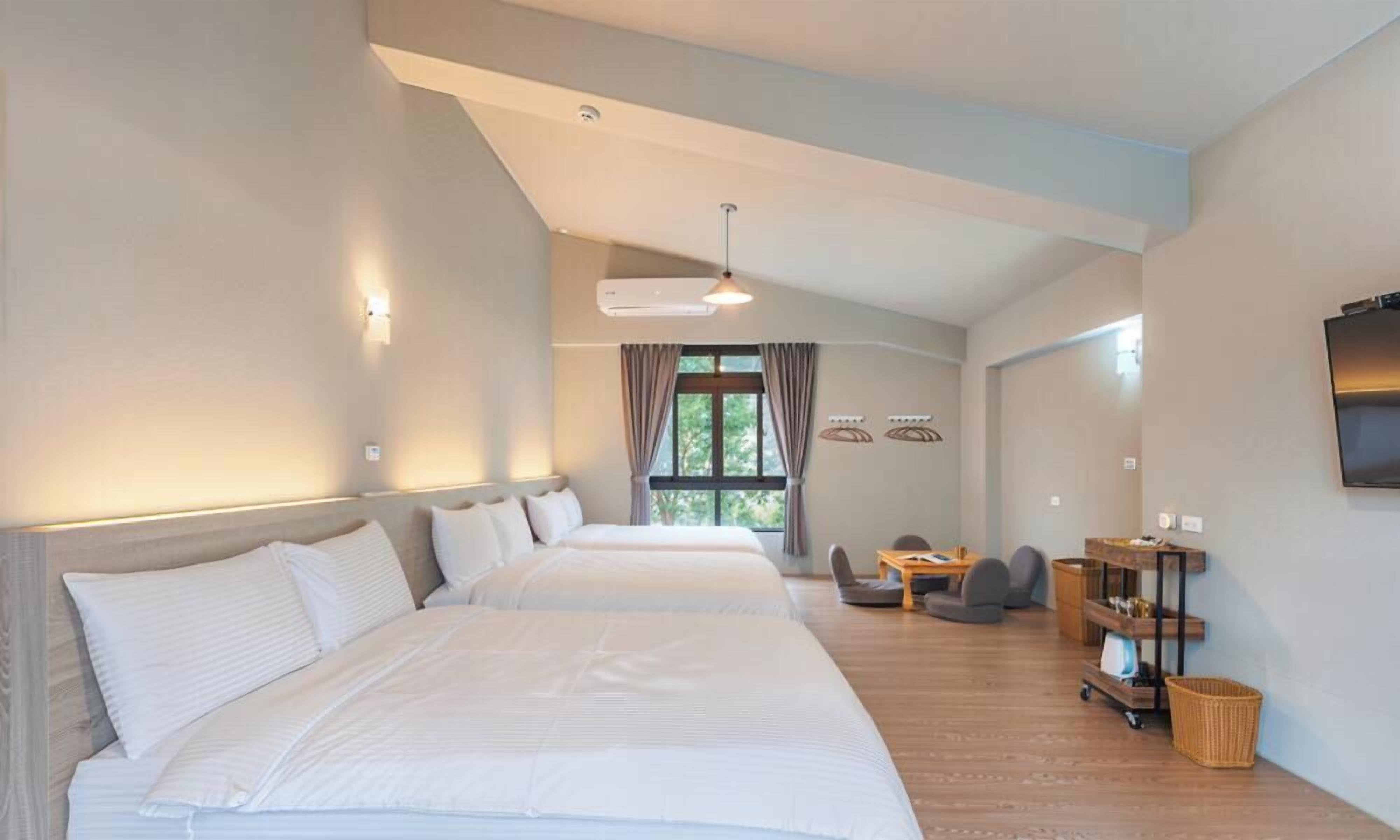 A hotel room with two beds, a desk, a chair, a TV, and a window with curtains.