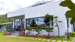 A modern building with large windows, a staircase, and a well-maintained garden with red flowers and bonsai trees. - Beluck (Luye)