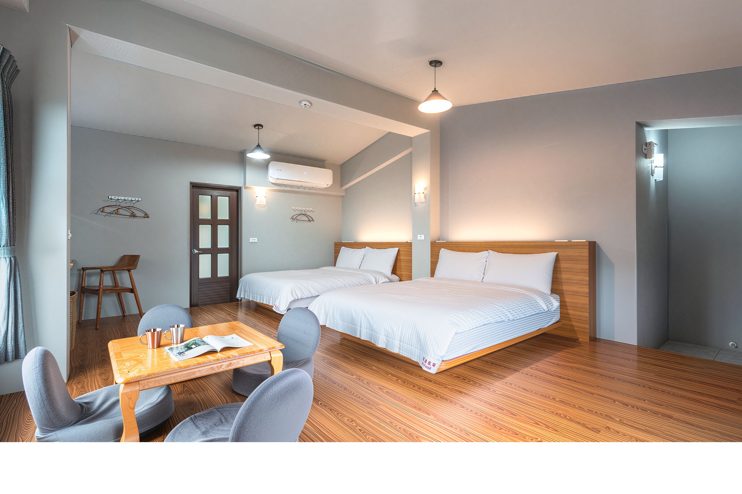 Une chambre avec deux lits, une table en bois avec des chaises, une porte et un appareil de climatisation.