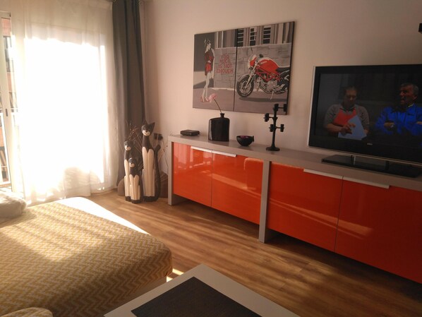 Een moderne woonkamer met een bank, een televisie, een rode kast en een schilderij van een motor.