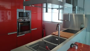 Una cocina moderna con armarios rojos, electrodomésticos de acero inoxidable y un ventanal que deja entrar luz natural.