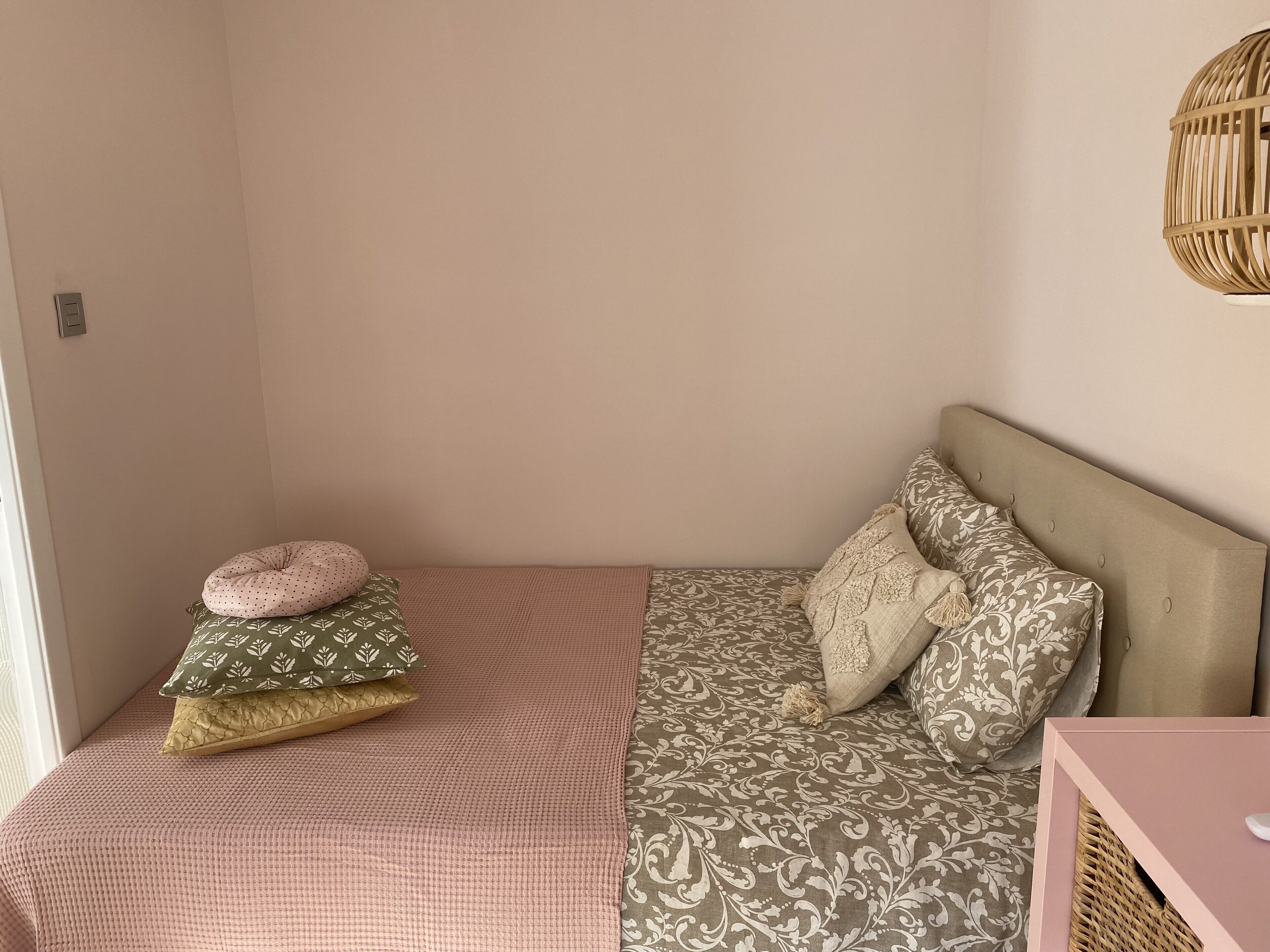 Un lit simple avec une literie à motifs et plusieurs oreillers, une table de chevet et un luminaire fixé au mur.