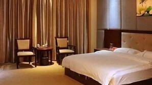 A hotel room with a large bed, two chairs, a small table, and a painting on the wall. - Wang Fu Hotel (Dehong)
