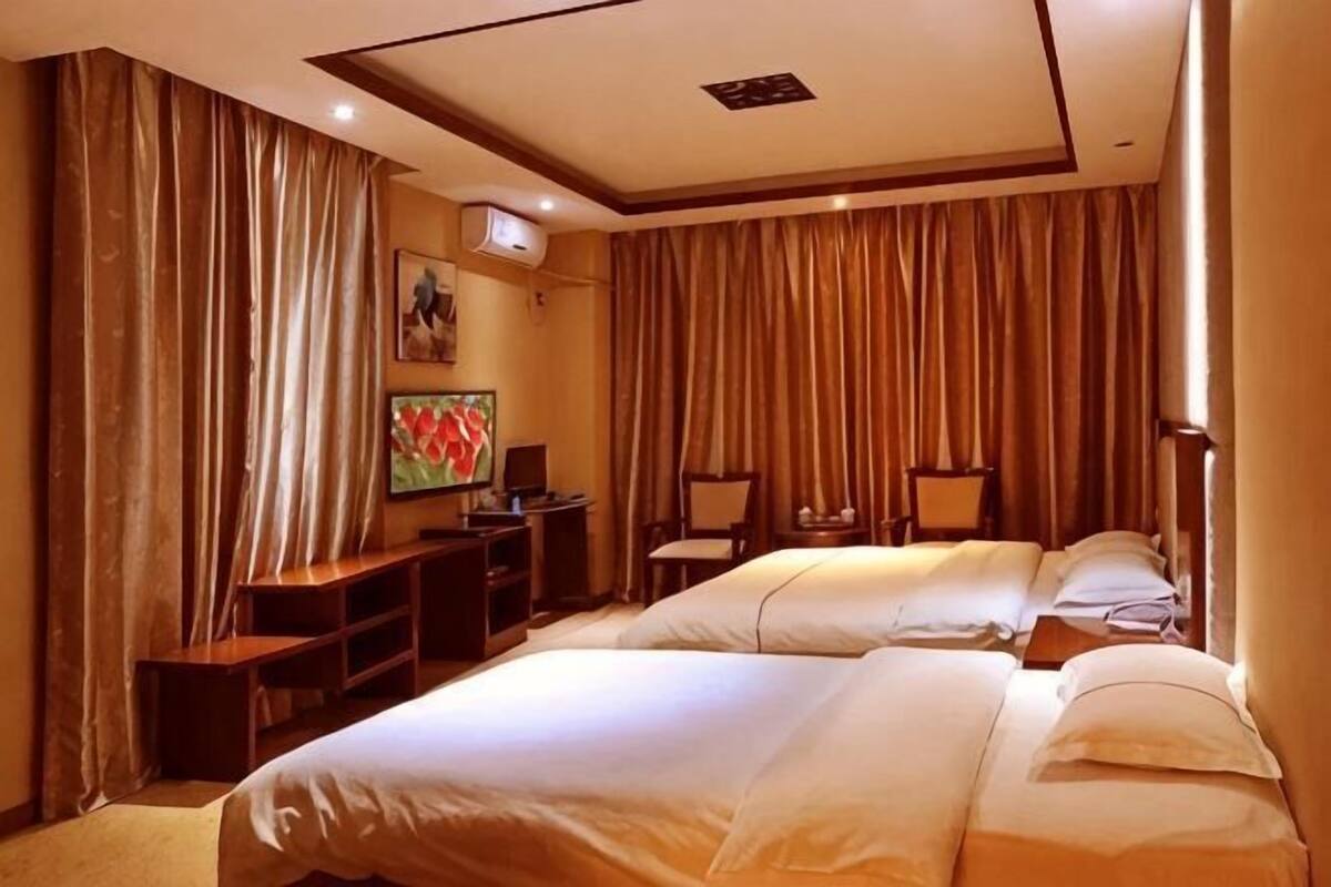 A hotel room with two beds, a desk, chairs, and a painting on the wall.