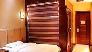 A hotel room with two beds, a large window with horizontal blinds, a wooden door, and a small bedside table. - Wang Fu Hotel (Dehong)