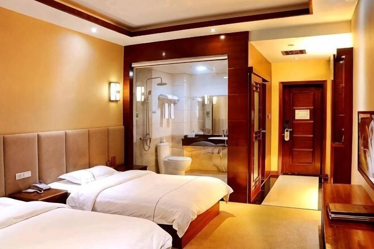 A hotel room with two beds, a bathroom with a shower, and a wooden door.