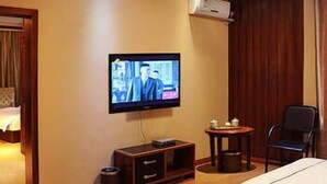 A hotel room with a bed, a television mounted on the wall, a small table with a chair, and an air conditioning unit. - Wang Fu Hotel (Dehong)