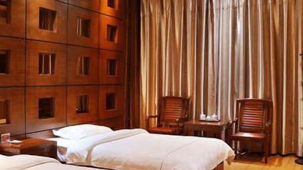 A hotel room with two beds, wooden paneling on the walls, a large window with curtains, and two wooden chairs. - Wang Fu Hotel (Dehong)