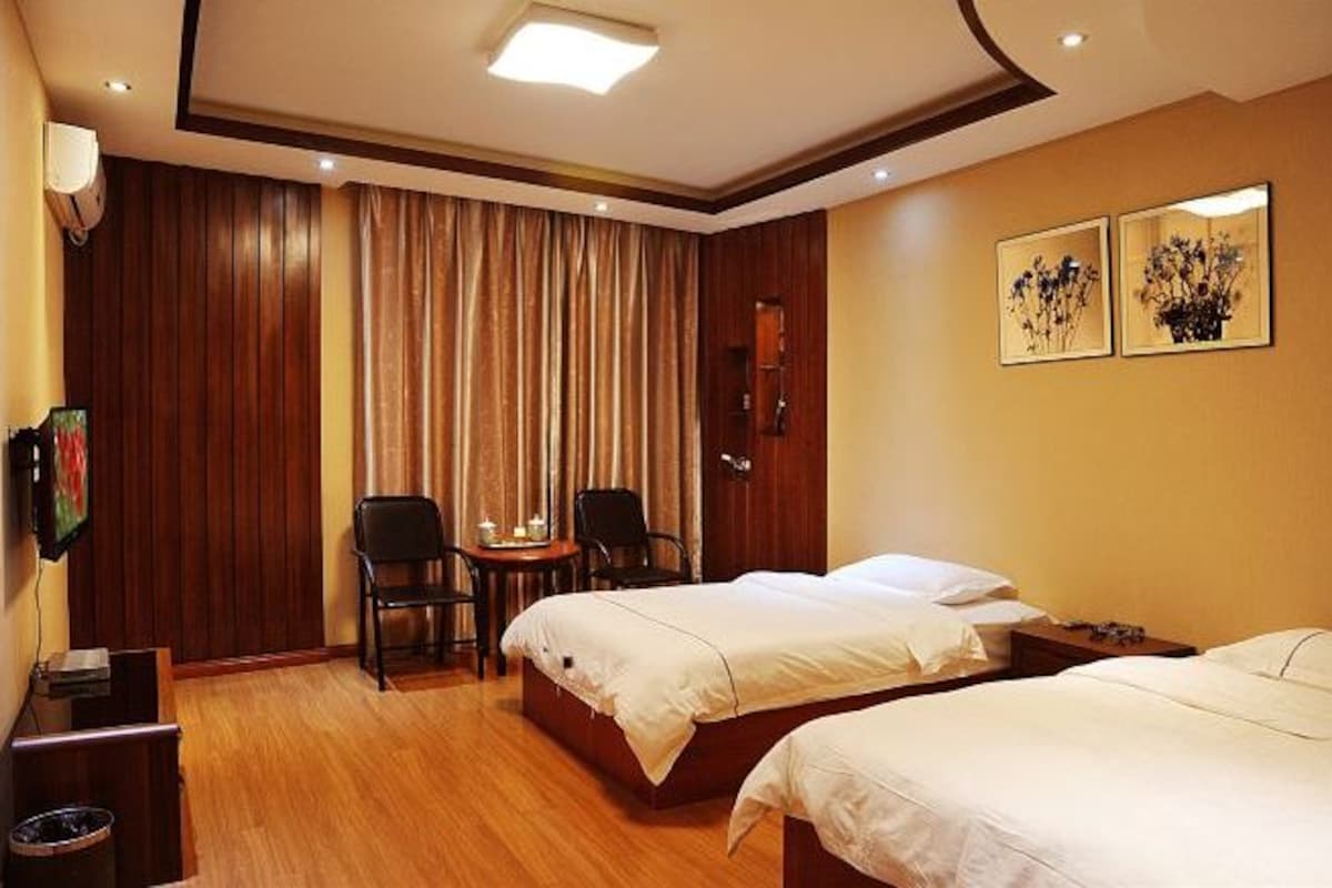 Habitación de hotel con dos camas, suelo de madera, escritorio con silla, televisor y dos cuadros en la pared.
