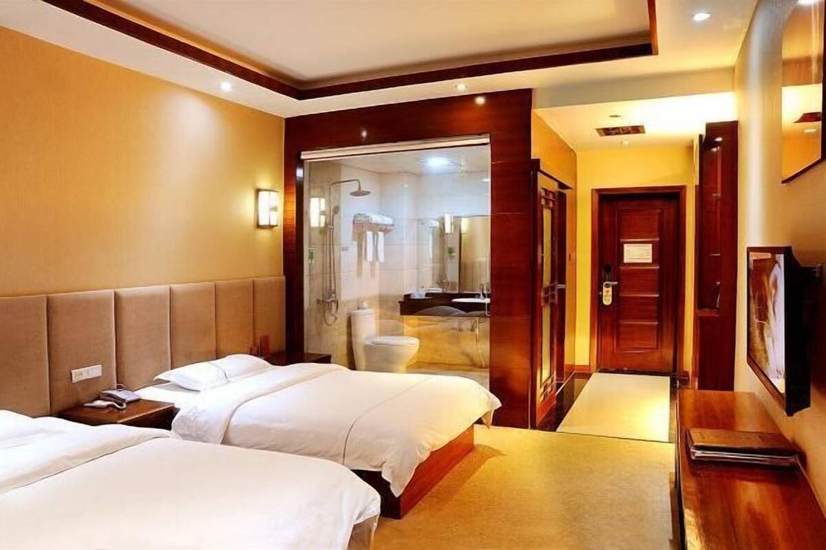 A hotel room with two beds, a bathroom with a glass shower enclosure, and a wooden door.