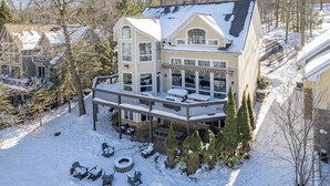 A large two-story house with a covered deck and a snow-covered yard. - Luxury Lakefront w/ Hot Tub & Rec Room (Oakland)