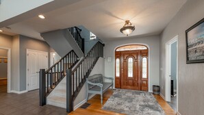 A spacious foyer with a wooden staircase, a bench, and a large wooden door with stained glass windows. - Luxury Lakefront w/ Hot Tub & Rec Room (Oakland)