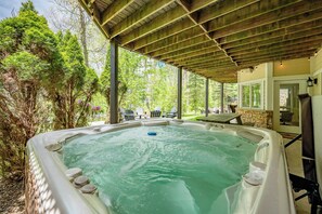 Banheira de hidromassagem sob pérgola de madeira, com vista para um jardim e mobiliário de exterior.