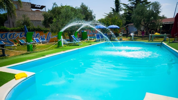 Une piscine avec des fontaines, entourée de pelouse verdoyante et d’arbres.
