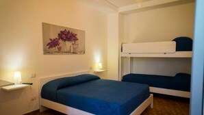 Une chambre avec un lit simple, un lit superposé, une table de chevet avec une lampe et un tableau accroché au mur.