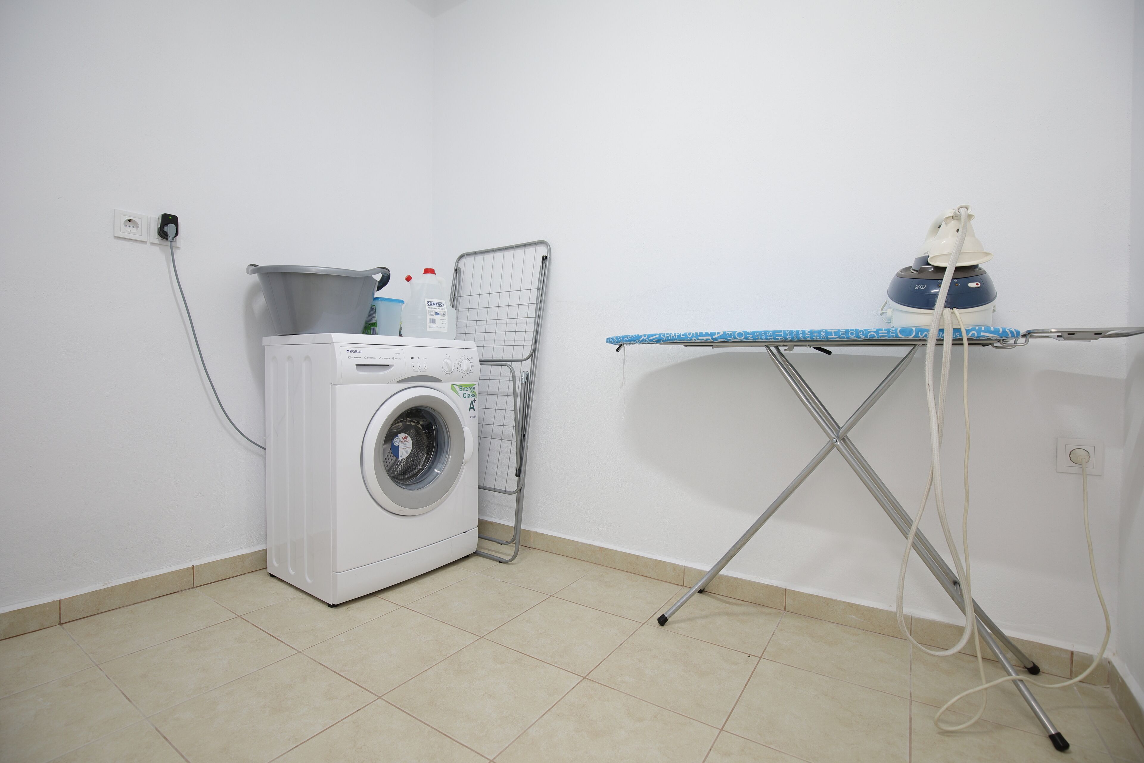 Een wasruimte met een wasmachine, een droogrek en een strijkplank.