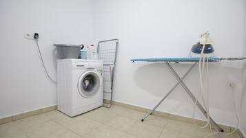 Een wasruimte met een wasmachine, een droogrek en een strijkplank.