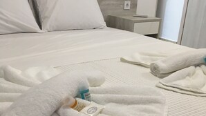 Un llit ben fet amb roba de llit i tovalloles blanques, un capçal de fusta, una tauleta de nit amb una làmpada i una porta de bany.