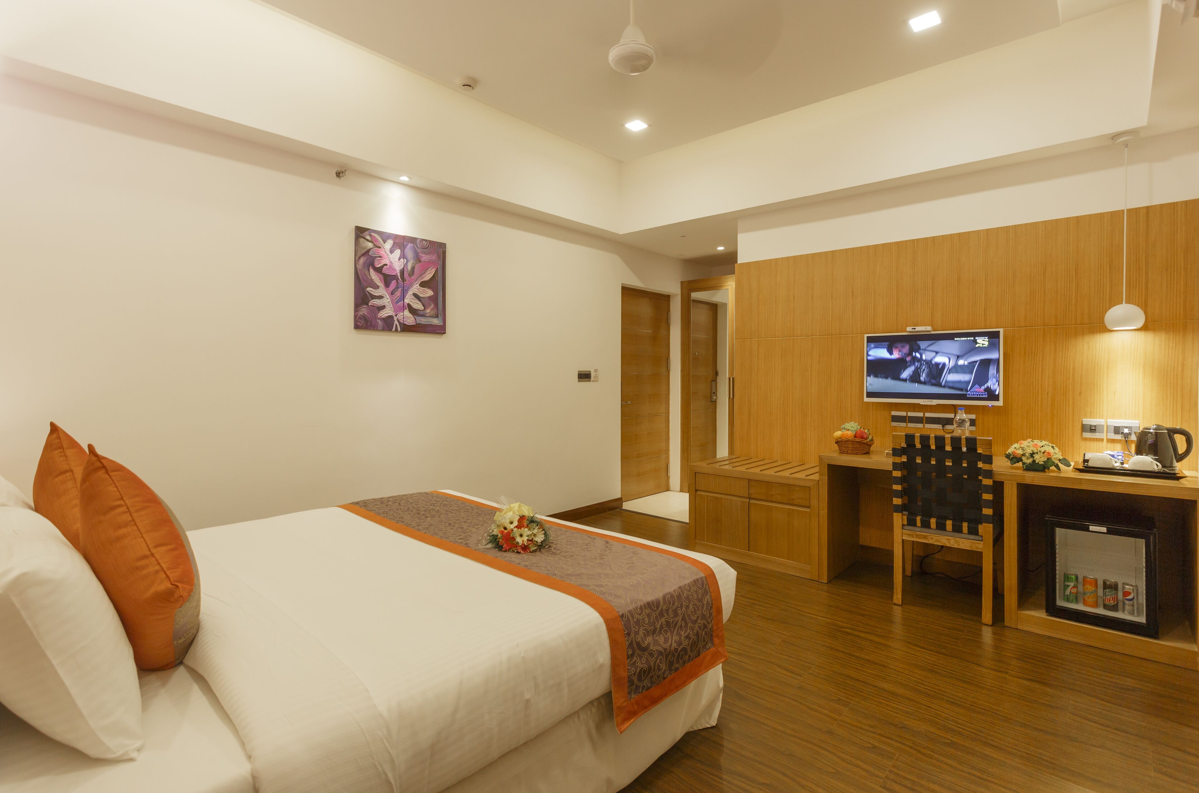 A hotel room with a bed, a desk, a television, and a kitchenette.