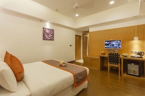 A hotel room with a bed, a desk, a television, and a kitchenette. - Medora Hotel (Kozhikode)