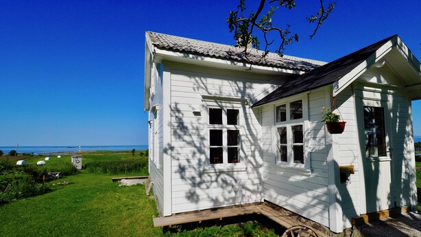 Et hvidt hus med en træterrasse og en vogn, omgivet af en græsplæne og en klar, blå himmel.