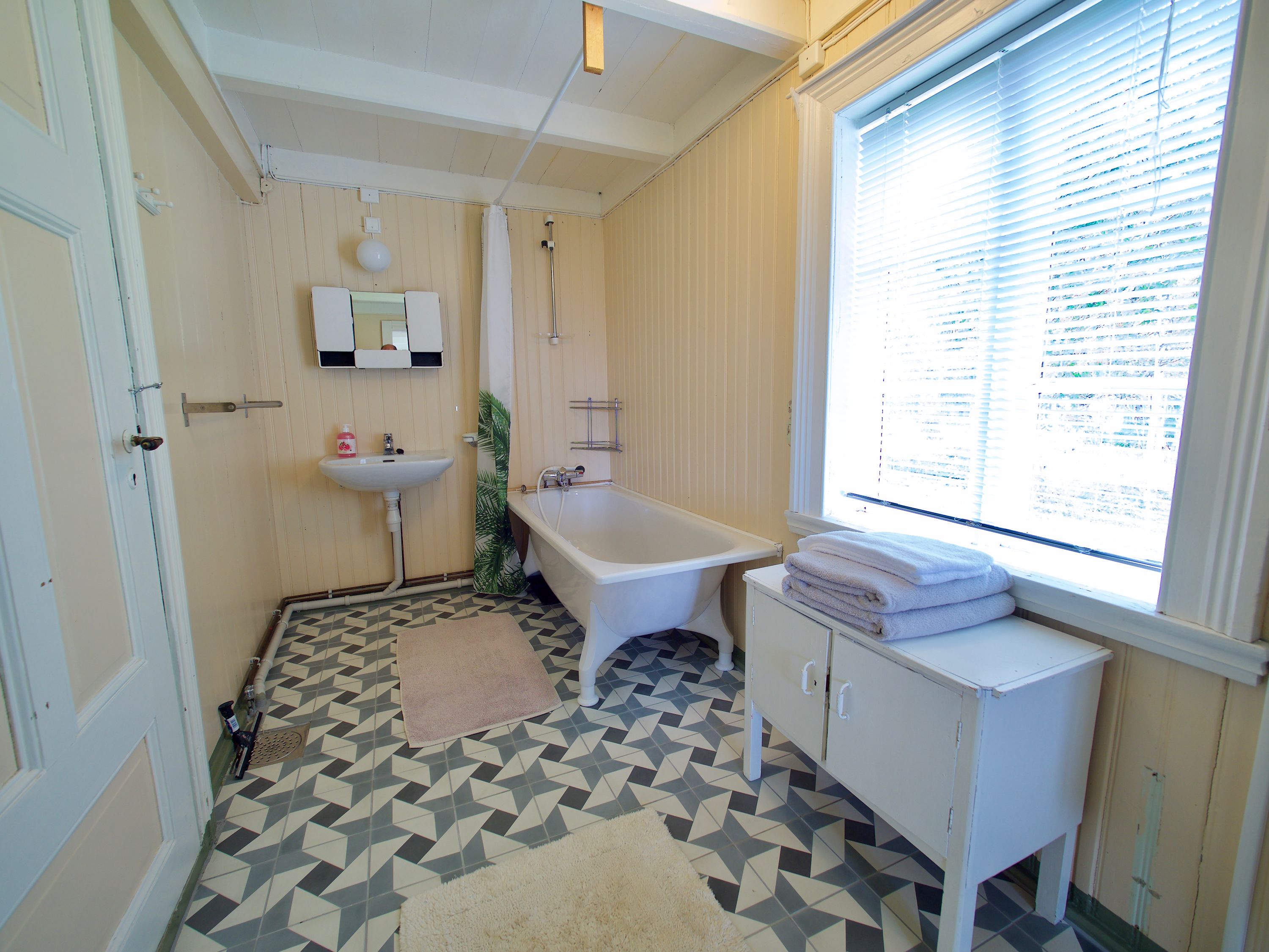 A bathroom with a bathtub, sink, and window with blinds.