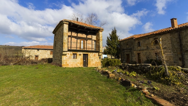 Un edificio de piedra con techo de tejas, un pequeño jardín y cielo despejado.