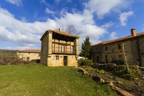 Un edificio de piedra con techo de tejas, un pequeño jardín y cielo despejado.