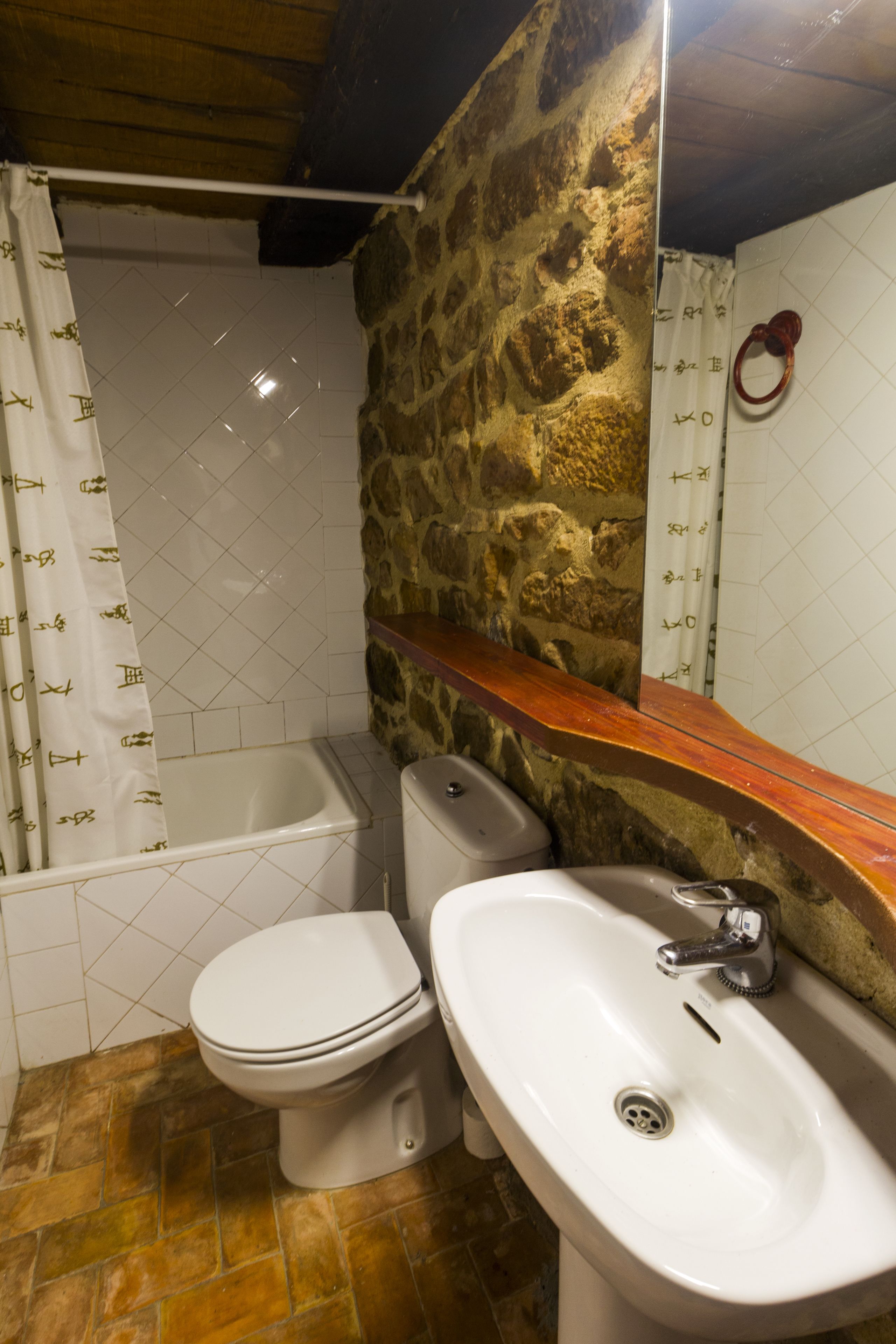 A bathroom with a stone wall, a white bathtub, a white toilet, and a white sink.