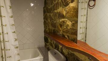 A bathroom with a stone wall, a white bathtub, a white toilet, and a white sink.
