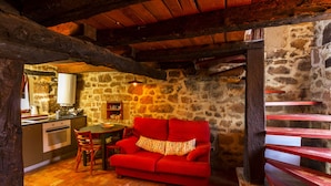 Una habitación rústica con paredes de piedra, techo de madera, un sofá rojo, una mesa de comedor de madera y una zona de cocina con estufa y fregadero.